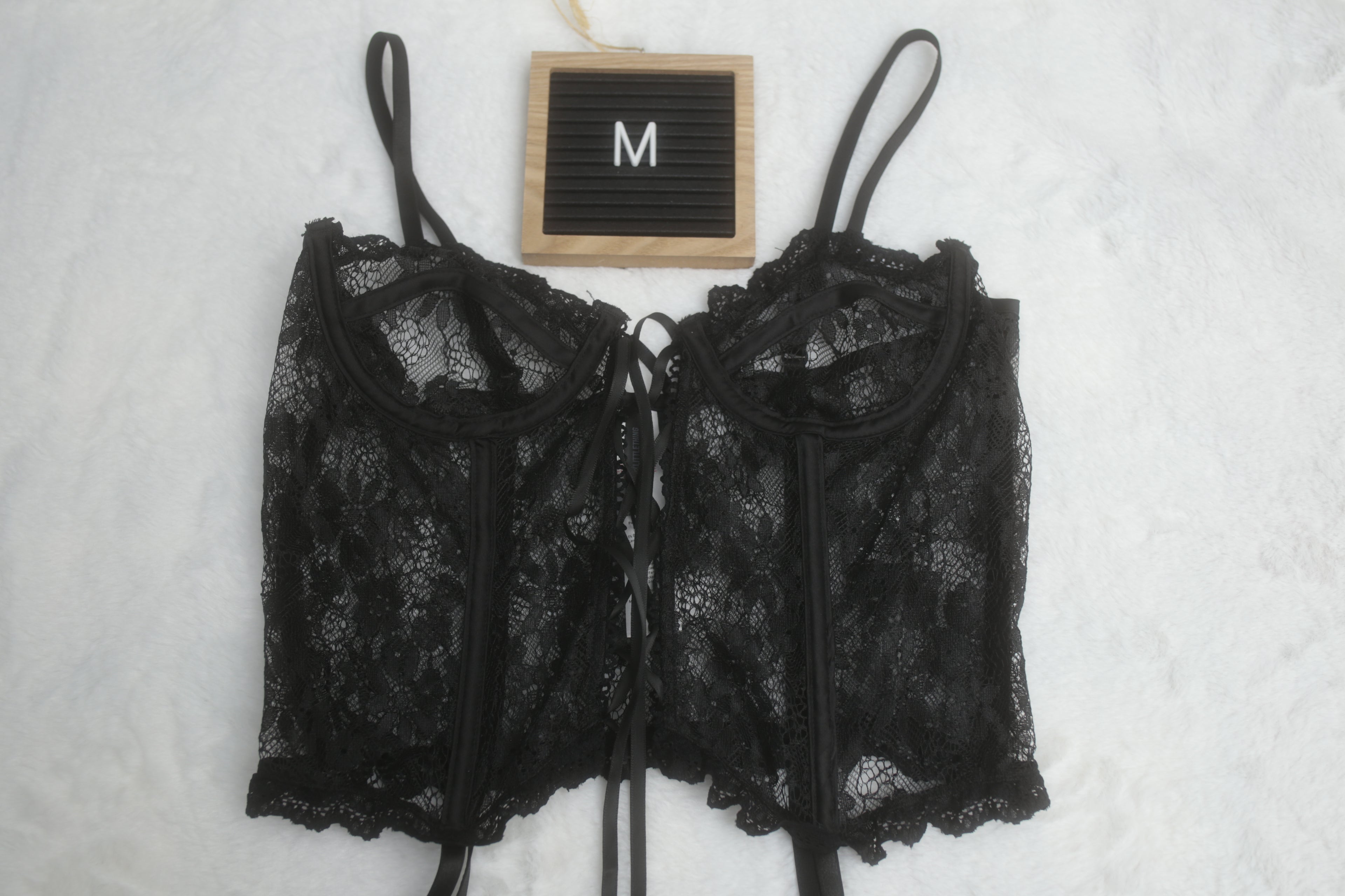 A black floral lace corset lingerie top with adjustable straps, attached garter straps, and underwire support. The letter 'M' indicates the size is medium.