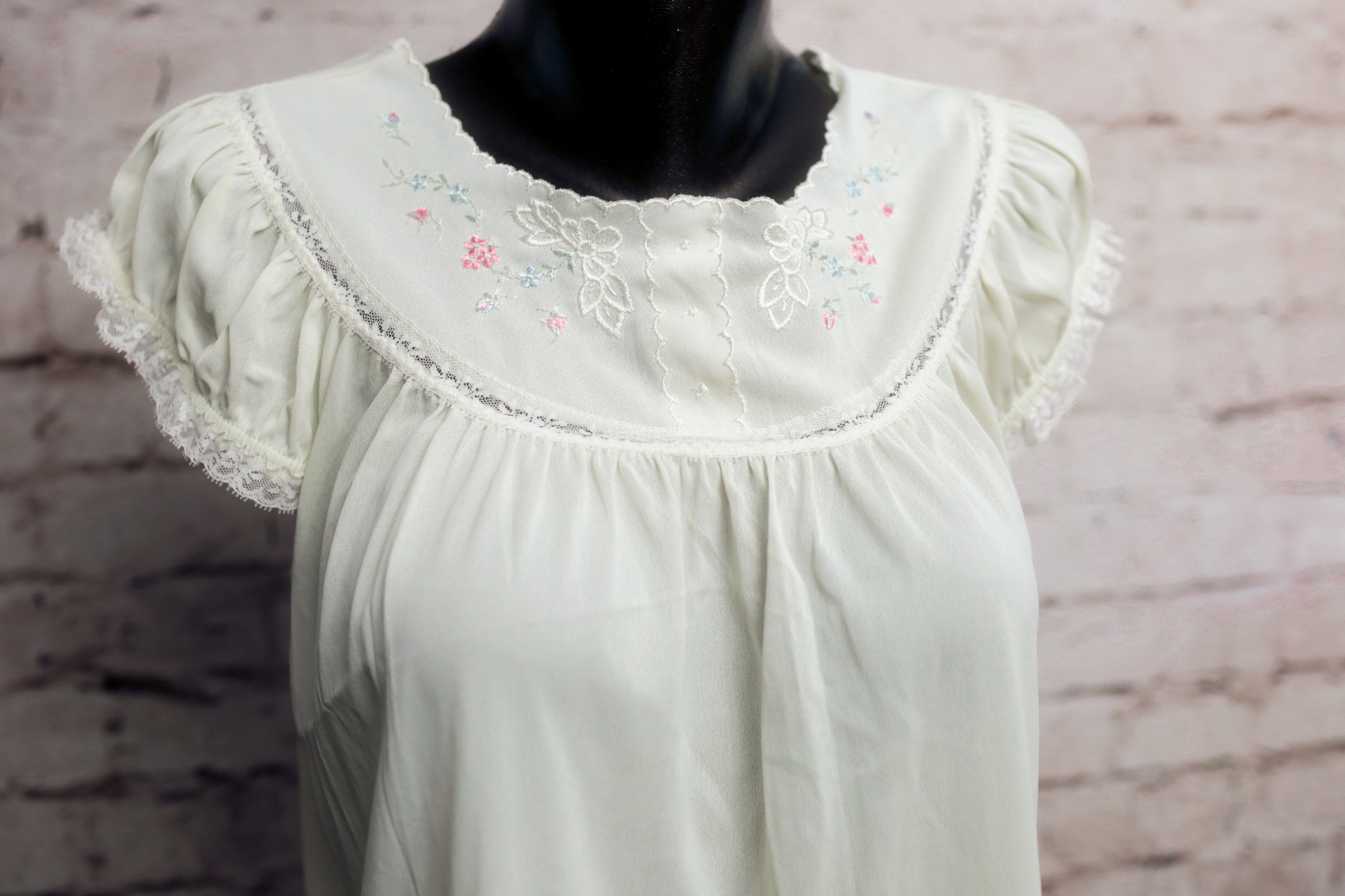 White blouse with embroidery on a mannequin against a brick wall background