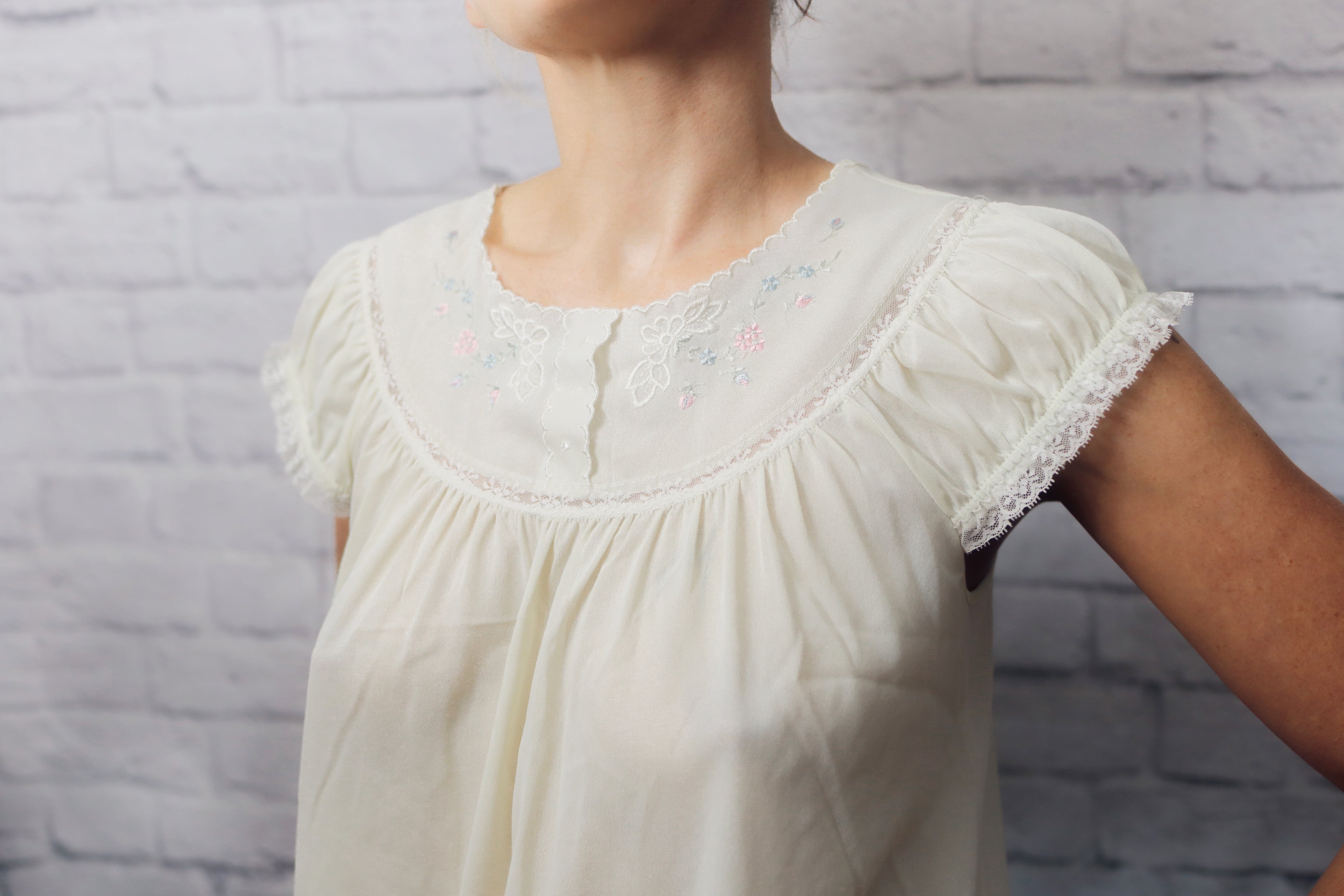 Light-colored blouse with lace details worn by a person against a gray brick wall.